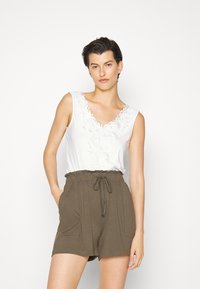 Top branco sem mangas com detalhe bordado em forma de V, combinado com calções verdes oliva com cordão na cintura, apresentando bolsos laterais e um corte descontraído.