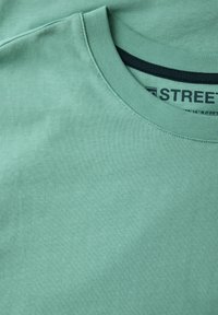 Camiseta verde menta con un clásico cuello redondo y mangas cortas. Textura suave y lisa con detalles de diseño mínimos.