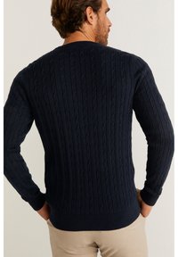 Mörkblå stickad tröja med flätstickad struktur, ribbade manschetter och midja. Utmärker sig med en figursydd design och långa ärmar.