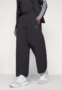 Pantalons de sport noirs avec une coupe décontractée et une taille élastique, présentant des poches latérales et un détail de logo subtil en gris foncé.