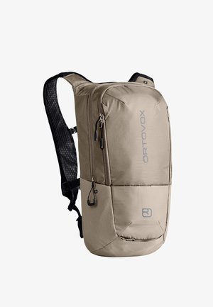 Kompakter beiger Rucksack mit gepolsterten schwarzen Schultergurten, mehreren Reißverschlussfächern und "ORTOVOX"-Schriftzug auf der Vorderseite.