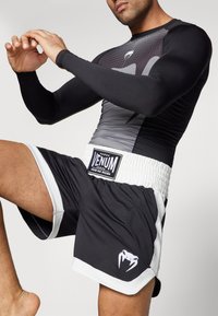 Svart og grå langermet rash guard med geometrisk mønster og hvite shorts som har strukturert midjebånd og logodetalj.