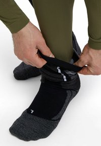 Des chaussettes de sport noires et grises remontées jusqu'à la cheville sur un legging vert, mettant en valeur un tissu texturé avec des couleurs contrastantes.