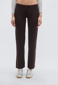 Pruunid venivad püksid nöörvöökohaga, sirgete säärete ja sileda tekstuuriga, kombineeritud hõbedaste tennistega.