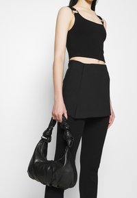 Schwarzes geripptes, kurzes Tanktop mit metallen Akzenten, kombiniert mit einem schwarzen strukturierten Minirock und einer ledernen Handtasche mit Knotenhenkel.