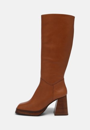 Wysoki brązowy skórzany but z kwadratowym noskiem i masywnym drewnianym obcasem typu klocek, gładkie wykończenie, wysokość do połowy łydki.