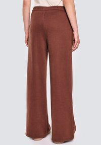 Szerokie brązowe spodnie dresowe z elastycznym pasem, wykonane z miękkiego materiału. Posiadają prosty design i gładką fakturę.