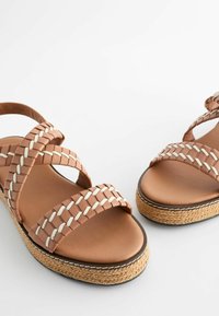 Brūnas austas sandales ar krustveida siksnām, platu espadrille stila jutu zoli un gludu beigu krāsas zoli.