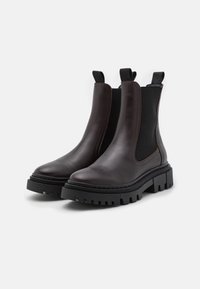 Brown leather Chelsea boots with black elastic side panels, chunky black rubber sole, and pull tabs for easy wear. Smooth texture, sleek design.