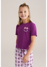 Camiseta de algodón morada con mangas cortas que presenta gráficos de flores. Combinada con pantalones de pijama estampados en rosa y blanco con acentos oscuros.