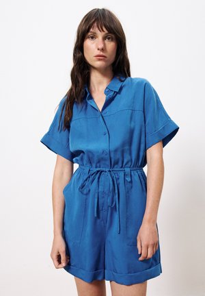 Combinaison bleue à manches courtes avec un devant boutonné, une taille cintrée et deux poches plaquées. Tissu doux avec une texture lisse et des poignets repliés.