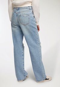 Jasnoniebieskie dżinsowe spodnie szerokie w nogawkach o wyblakłej fakturze, z delikatnym przetarciem na końcach nogawek i dwiema tylnymi kieszeniami. Noszone z białą bluzką i beżowymi butami.