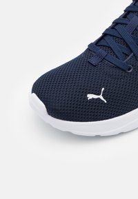 Bottines de course en maille marine avec un logo blanc sur le bout, surface texturée et une semelle blanche légère au design arrondi.