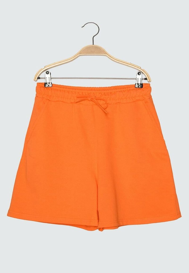 Shorts orange à taille élastique avec cordon, suspendus sur un cintre en bois sur fond uni.