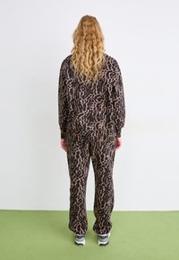 Set za udobno nošenje s leopardjim vzorcem v rjavi in črni barvi, ki vključuje ohlapen zgornji del in hlače. Mehka tekstura, elastičen pas in stranske žepke.