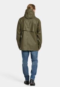 Vattenavvisande jacka i olivgrönt med huva, utrustad med ventilationsöppning bak och slät yta, kombinerad med blå jeans och svarta stövlar.