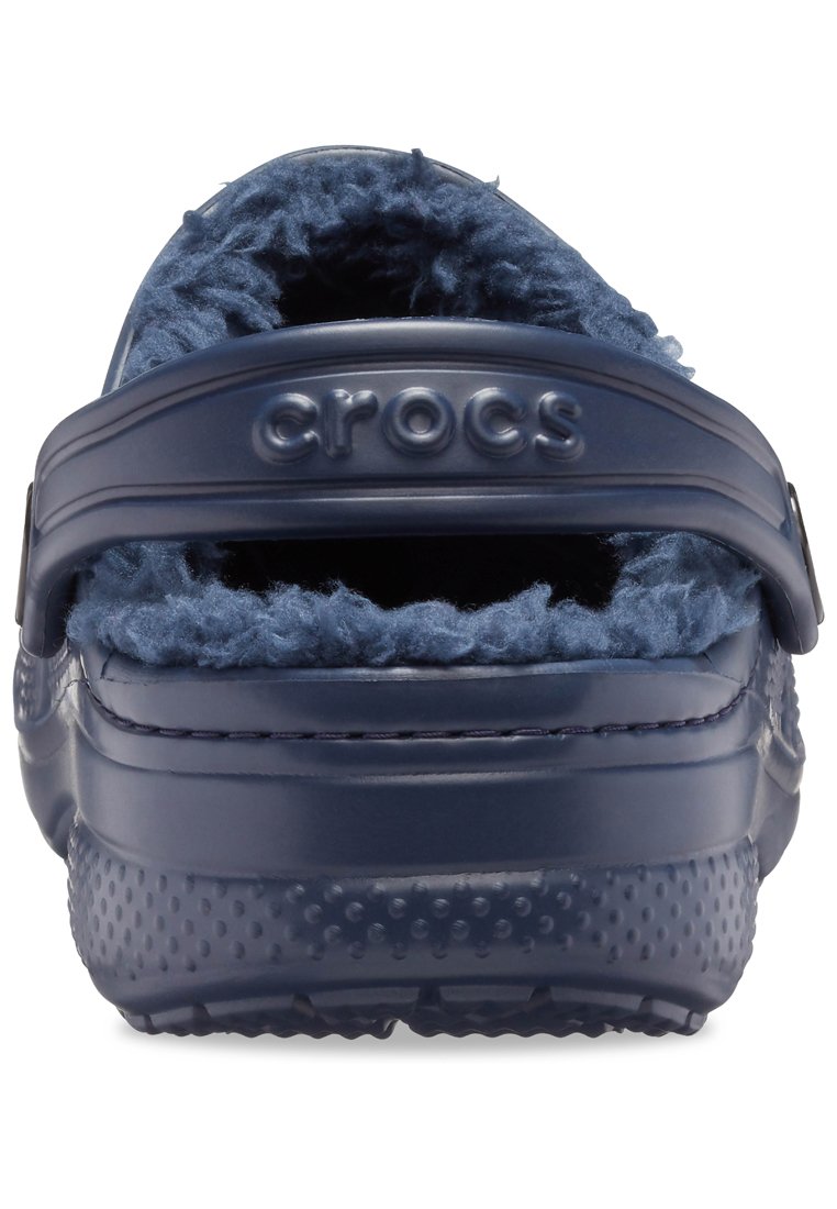 Crocs di colore blu navy con una morbida fodera pelosa, una larga cinghia con l'etichetta "crocs" e una suola esterna texturizzata e punteggiata per una migliore aderenza.
