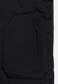 Sezione di giacca a vento nera con tasca con zip, superficie liscia, leggero luccichio e dettagli cuciti sul tessuto.