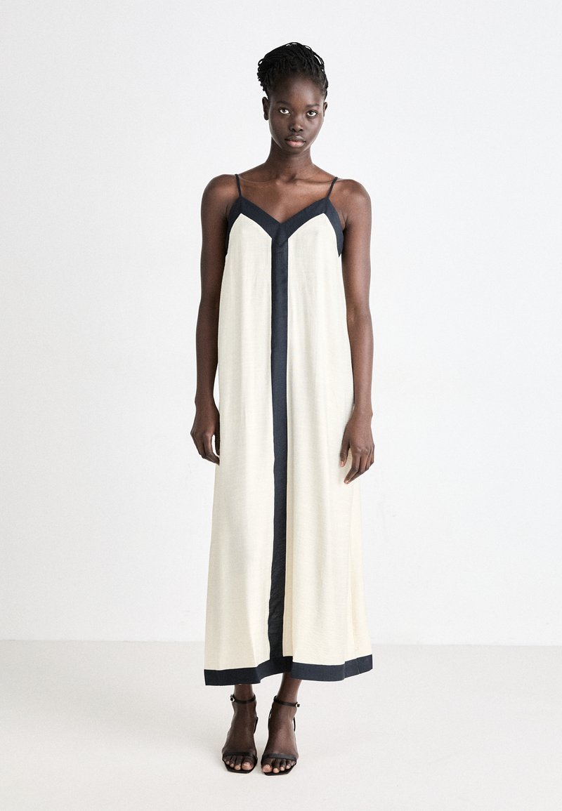 Langes, ärmelloses Kleid in Creme mit dunkelblauen Akzenten entlang des V-Ausschnitts und Saums. Hergestellt aus leichtem Stoff, mit geradem, lockeren Schnitt.
