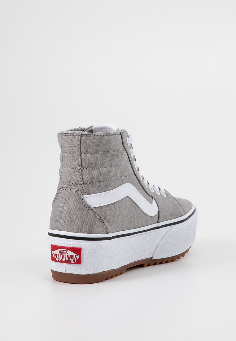 Zapatilla alta en lienzo gris con una franja blanca, suela de goma negra y blanca, y logotipo de Vans en rojo. Presenta un collar acolchado y cordones planos.