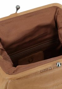 Intérieur d'un sac à main en cuir marron avec une texture lisse, une poche zippée et un patch avec logo en relief. Le fermoir est en métal et de forme ronde.