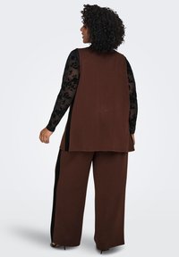 Brown sleeveless top paired with black floral long-sleeve shirt, featuring wide-leg brown pants with black side accents. Textured fabric.