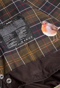 Ύφασμα Barbour σε καρό σχέδιο με σκούρο πράσινο, μαύρο και κόκκινο. Περιλαμβάνει ετικέτα φροντίδας και εκτυπωμένο σχέδιο με πουλάκι ρομπίν.