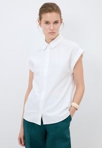 Witte kortgerafelde overhemd met puntkraag, gemaakt van lichtgewicht stof, gecombineerd met teal broek en een beige armband.