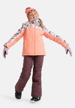 Veste matelassée pêche avec des manches à motifs, associée à un pantalon de neige bordeaux et des bottes noires. Accompagnée d'un bonnet en tricot orange et de gants.