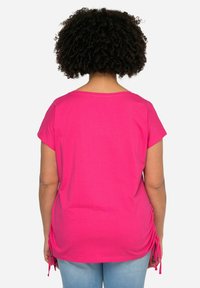 Top fucsia de manga corta con escote redondeado, que presenta lazos laterales para ajustar. Tejido de algodón suave, corte relajado y diseño sencillo.