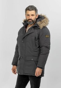 Grå polstret parka med hætte foret med pels, to frontlommer og knaplukninger. Har et logopatch på ærmet.