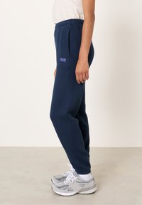 Tmavomodré teplákové nohavice z mäkkej látky s zúženým strihom, bočnými vreckami a logom "American Vintage" na prednej strane.