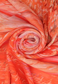 Un tessuto leggero, arancione e rosa, a motivo, arrotolato con cura, che mostra disegni astratti con vari toni e texture.