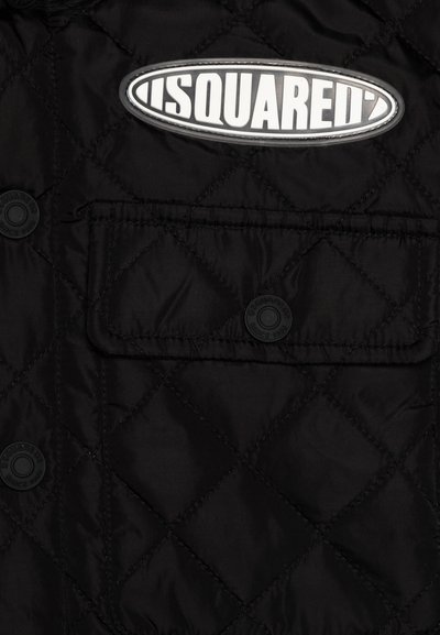 Gilet imbottito nero a quadri con un grande patch bianco con logo e chiusura a bottoni a pressione. Include una tasca sul petto con un bottone visibile.