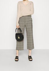 Pull beige en V, pantalon large à carreaux gris, sac à main noir avec détails en métal, et sandales noires à boucle.