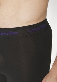 Calvin Klein zwarte leggings hebben een aansluitend ontwerp met een gladde textuur en een paarse logo band rond de taille voor merkindentificatie.