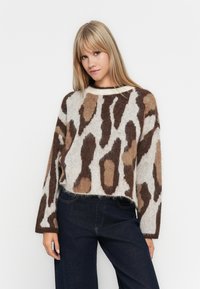 Knit sweater in cream, brown, and tan with a loose fit, featuring an animal print pattern and a round neckline. Long, wide sleeves.