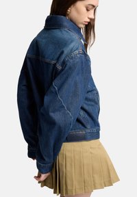 Kurtka dżinsowa o klasycznym kroju, ciemnoniebieskim kolorze i teksturowanej tkaninie. Wyposażona w kieszenie oraz skórzany detal z logo przy dolnym brzegu.