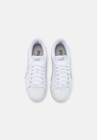 Baskets en cuir blanc avec une texture lisse, bout rond, lacets et branding Puma sur la languette, présentant un design minimaliste et des accents gris.