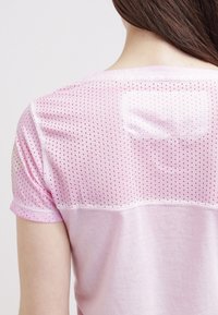 Rosa t-shirt med perforerat meshuvud och solid underdel, kortärmad med rund halsringning.