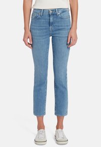 Jeans in denim azzurro chiaro con taglio dritto, vita media, cinque tasche e caviglie orlate, abbinati a scarpe da ginnastica bianche.