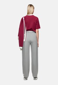 Maroonfarbene übergroße T-Shirt mit weißen Abschlüssen, kombiniert mit hellgrauen, vertikal gestreiften, weit geschnittenen Hosen und schwarzen Sneakern. Rückansicht.