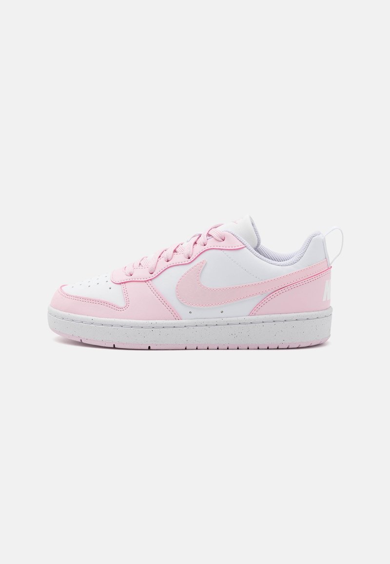 Baskets basses Nike blanches et roses avec semelle blanche mouchetée, laçage et logo Nike sur le côté et la languette du talon.