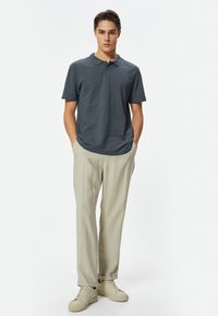 Dunkelgraues Polohemd mit Kragen, kombiniert mit hellbeigen Hosen und cremefarbenen Sneakers. Einfaches Design mit lässiger Passform und kurzen Ärmeln.