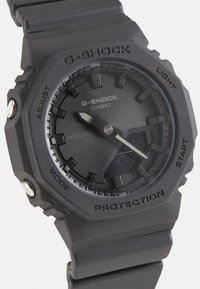 Ρολόι G-SHOCK με μαύρη ρητίνη περιβλήματος, υφασμένης επιφάνειας, λευκούς δείκτες και ψηφιακή οθόνη. Διαθέτει έντονους δείκτες ωρών και κουμπιά για λειτουργικότητα.