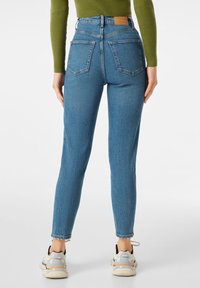 Högmidjade blå denimjeans med bakfickor, ljus blekning och rak passform. Bärs med grå och vita sneakers.