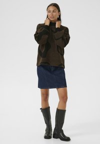 Brown patterned sweater with high neck, paired with a dark denim skirt. Black knee-high boots with textured finish. Simple background.
