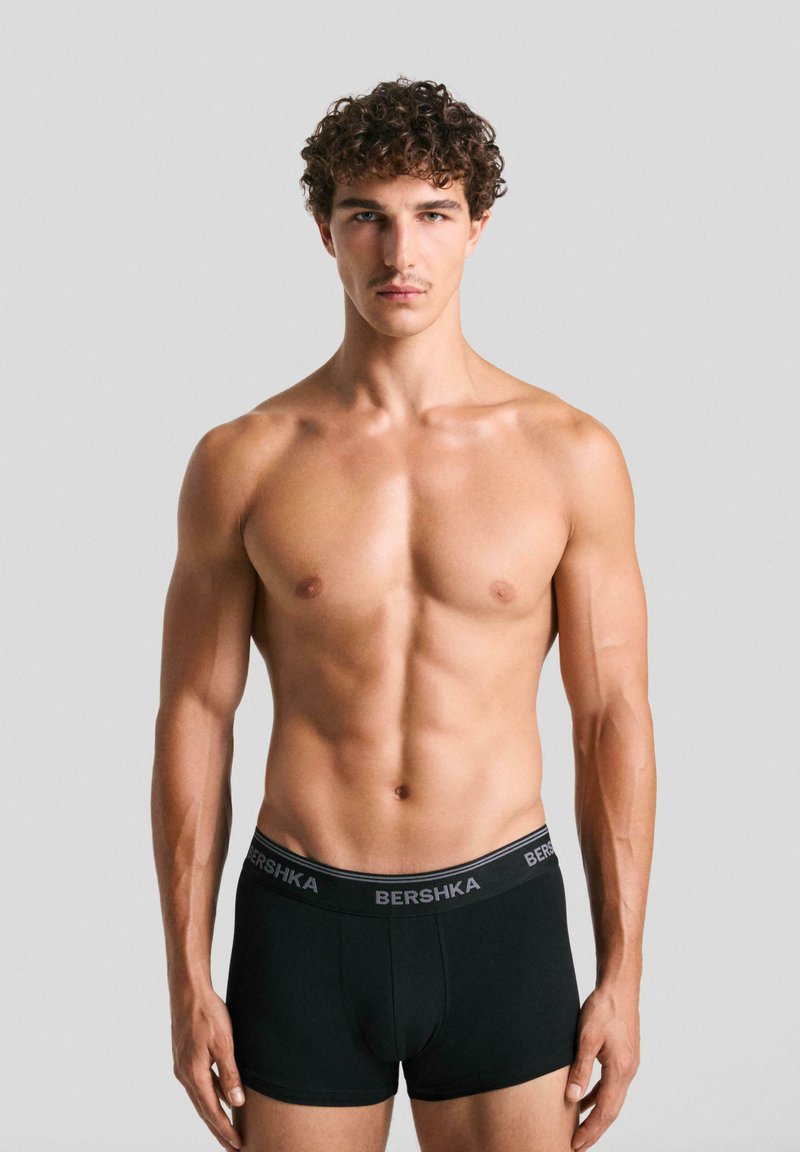 Boxer da uomo neri con elastico BERSHKA. Il tessuto appare liscio ed elastico. Il modello è senza maglietta, esibendo un fisico tonico.