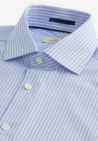 Hellblau-weiß gestreiftes Hemd mit Button-Down-Kragen, ausgestattet mit weißen Knöpfen und einer glatten Stoffstruktur. Pflegeetikett sichtbar.