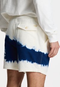 Pantalones cortos de algodón con un patrón de tie-dye, combinando blanco roto y azul marino, con un bolsillo trasero y una etiqueta de marca sutil.